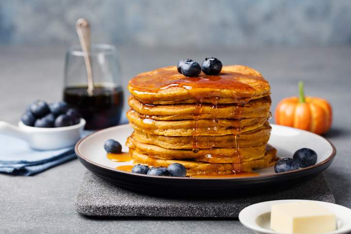 Pumpkin pancakes with maple syrup and blueberries on a plate.